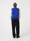 A male model showcases the Universal Works Blue Wool Fleece Zip Waistcoat worn unzipped over layers against a neutral studio background. The image highlights the open-front styling, relaxed fit, and cozy wool fleece material.