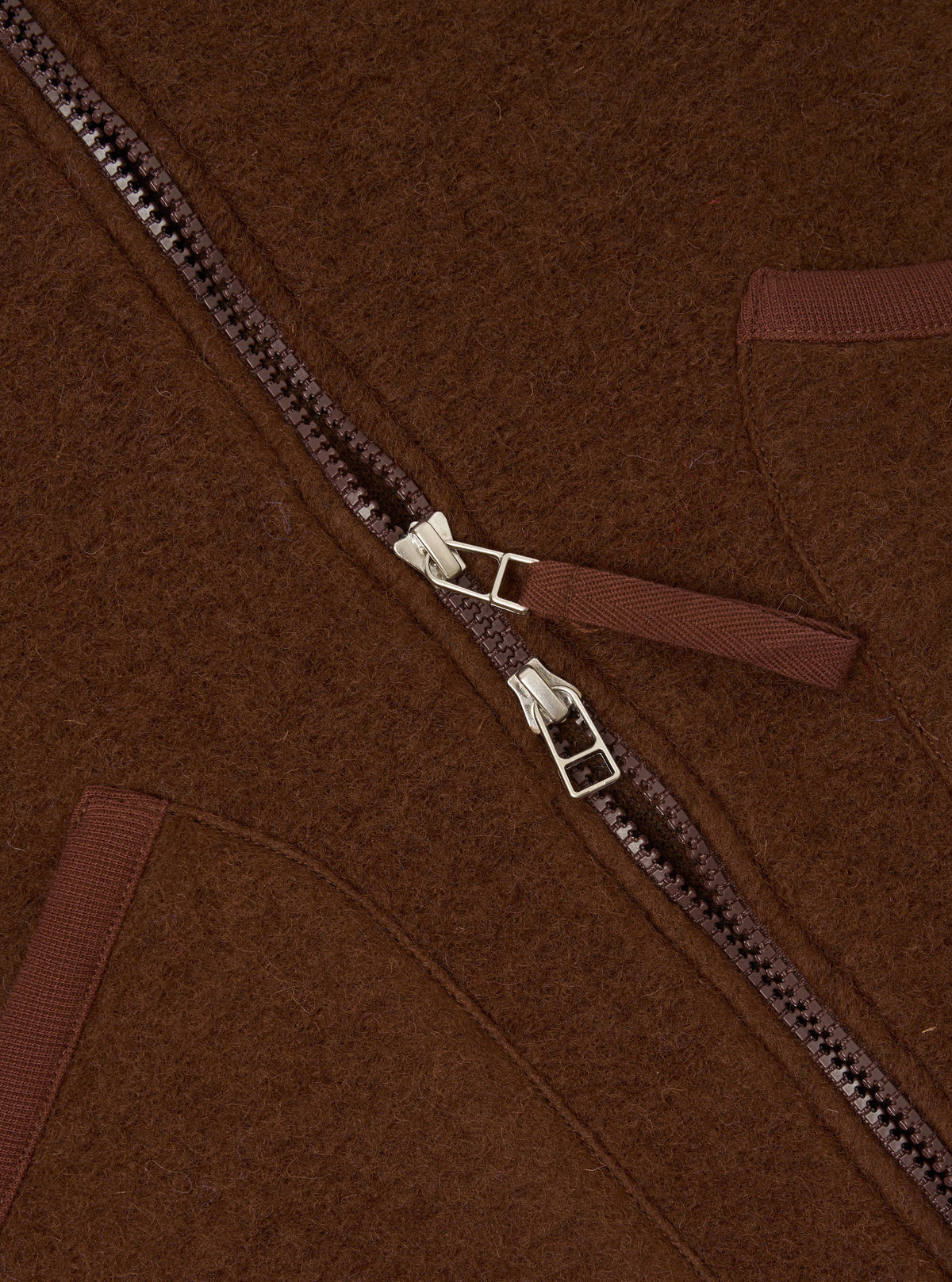 Close-up detail shot of the Cacao Wool Fleece Zip Waistcoat on a plain background. Focuses on the metallic front zipper hardware, rounded collar edge, and rich cacao brown fleece texture of the garment.