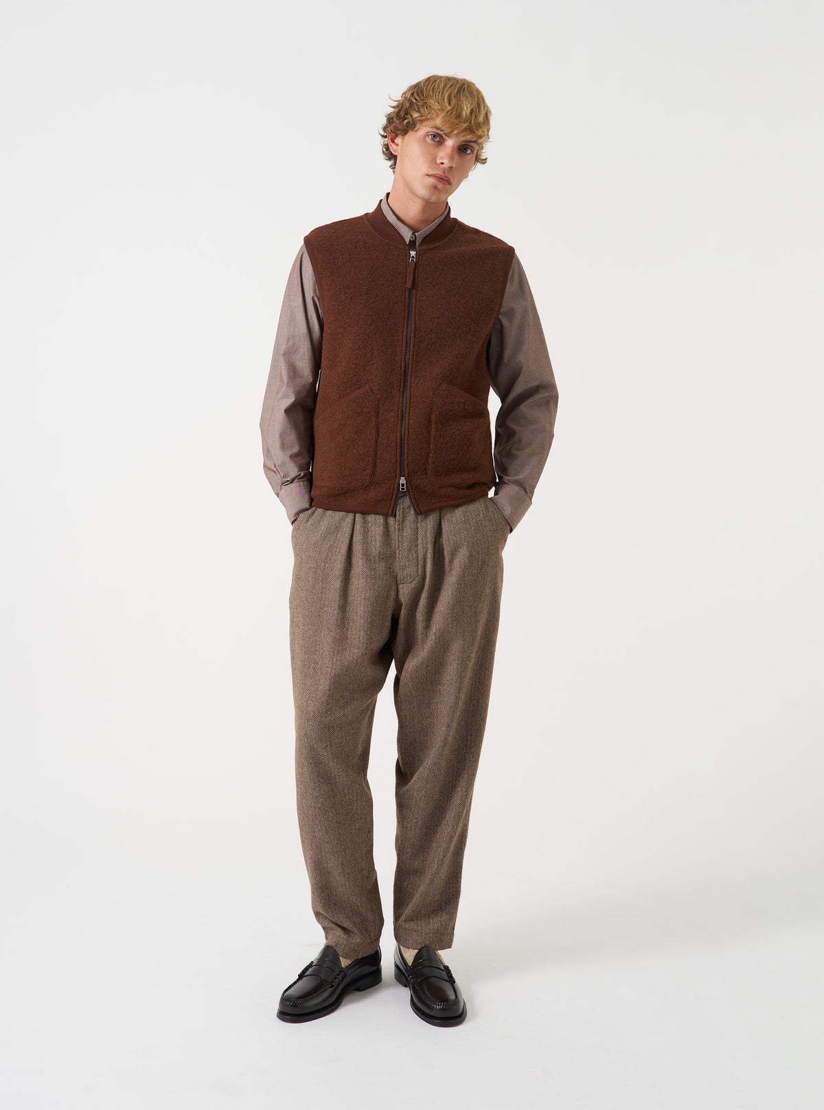 Front view of a model wearing the Cacao Wool Fleece Zip Waistcoat layered over a top in a studio setting with a light backdrop. The model stands facing forward, showing how the brown fleece waistcoat fits.
