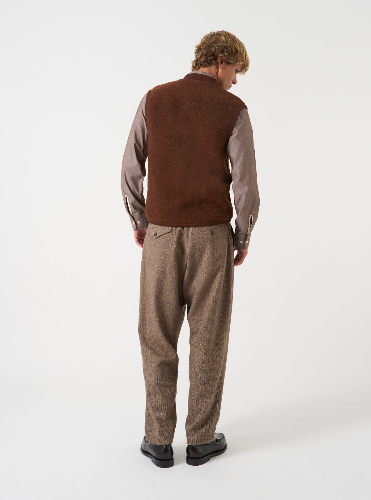 Angled view of a model wearing the Cacao Wool Fleece Zip Waistcoat in a plain studio setting. The shot demonstrates the garment fit from the side, highlighting the armhole cut and cacao brown wool fleece texture.