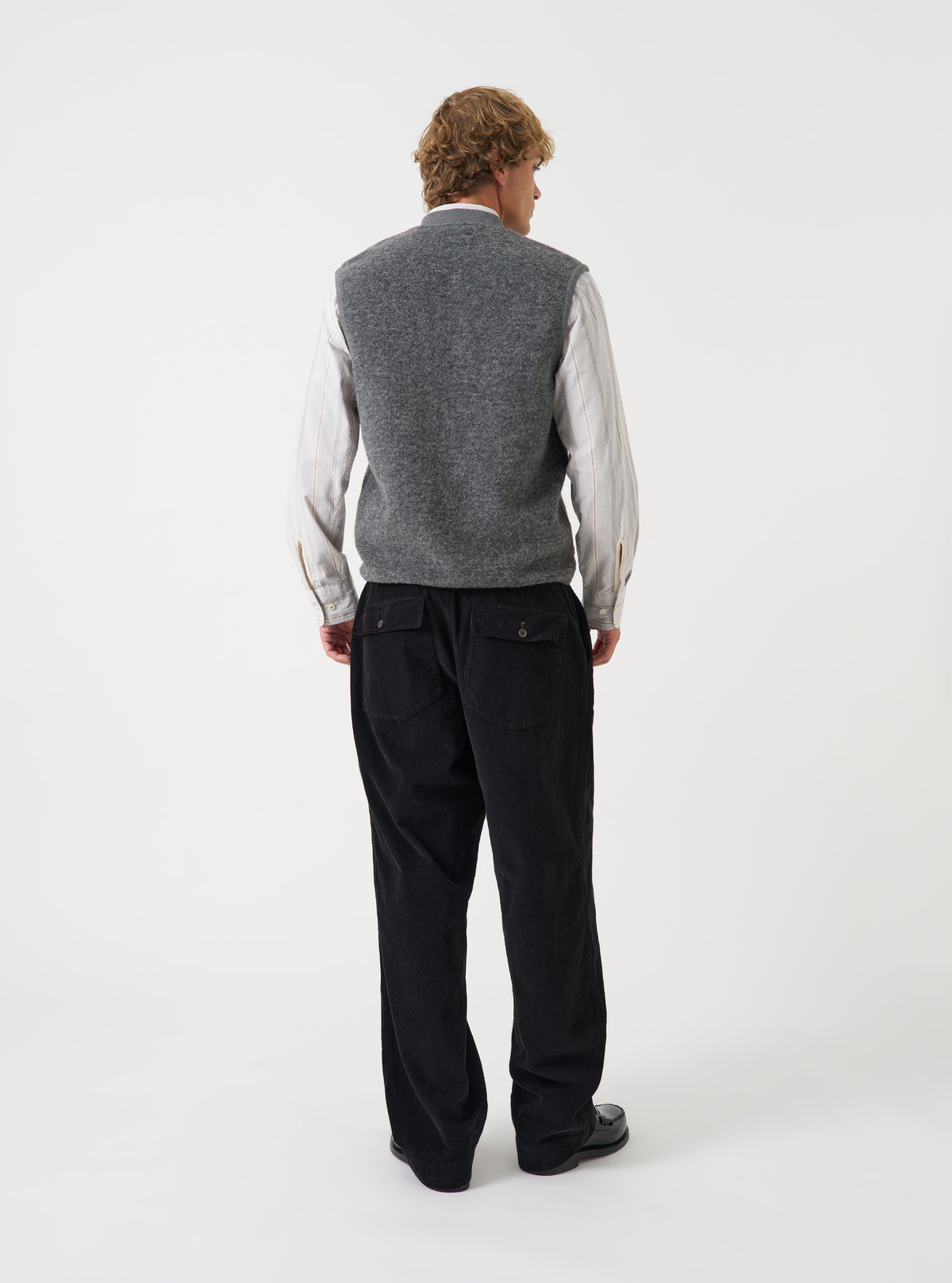Angled view of a model wearing the Grey Marl Wool Fleece Zip Waistcoat in a plain studio setting. The shot demonstrates the garment fit from the side, highlighting the armhole cut and grey marl wool fleece texture.