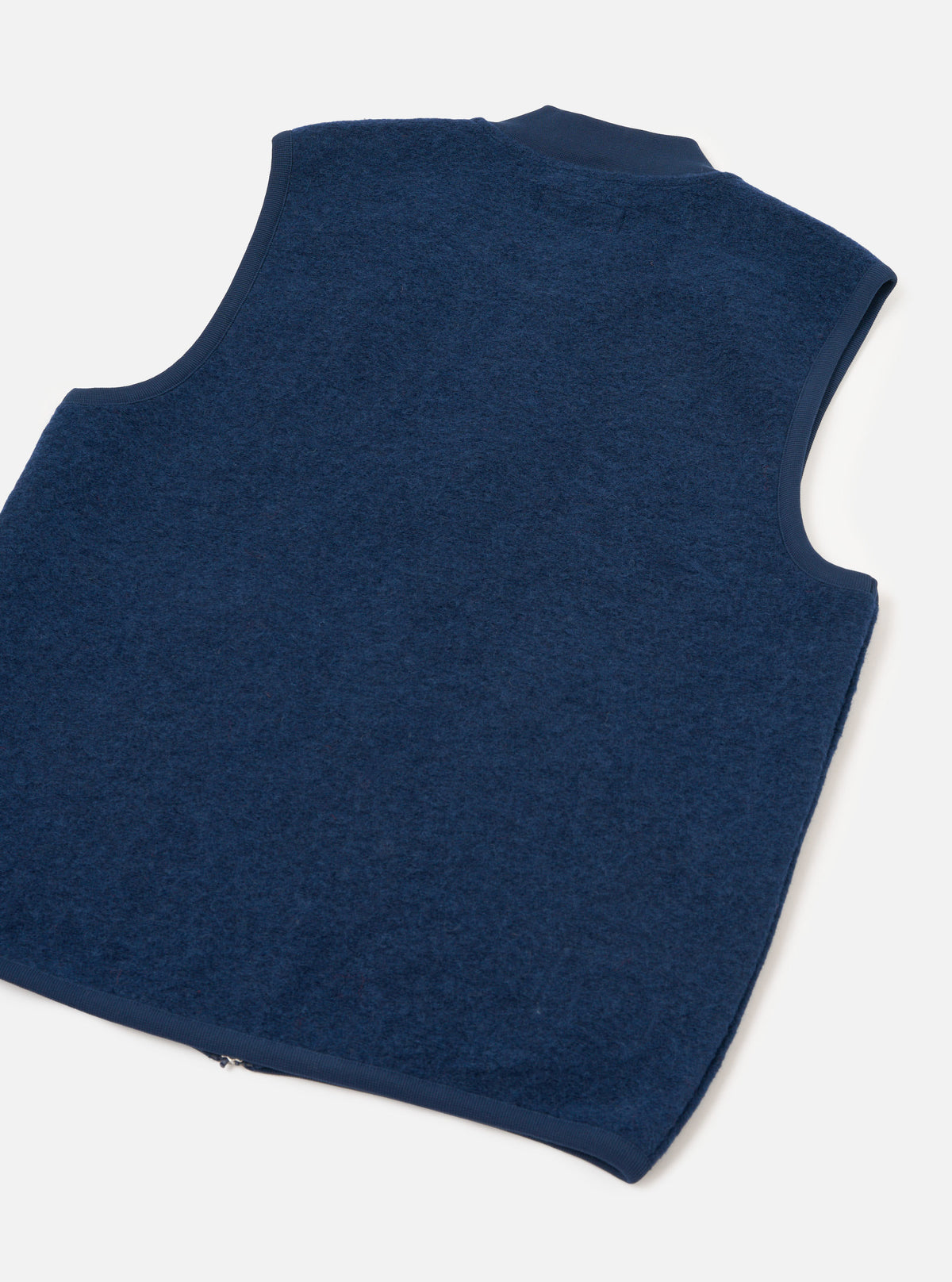 Rear view of the Indigo Wool Fleece Zip Waistcoat presented against a plain white background. The back section highlights the soft indigo blue wool fleece texture, clean hemline, and simple sleeveless construction.