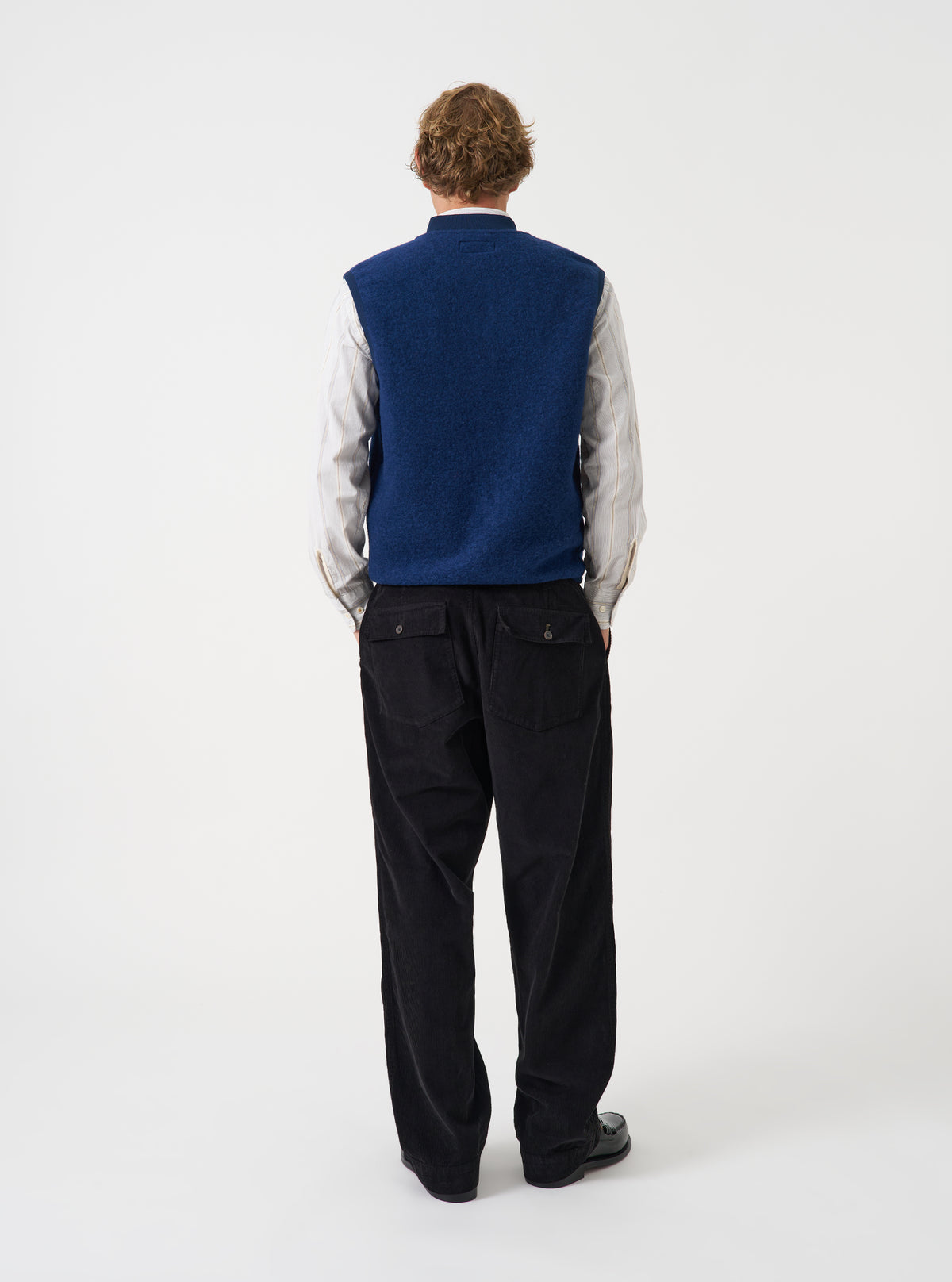 Angled view of a model wearing the Indigo Wool Fleece Zip Waistcoat in a plain studio setting. The shot demonstrates the garment fit from the side, highlighting the armhole cut and indigo wool fleece texture.