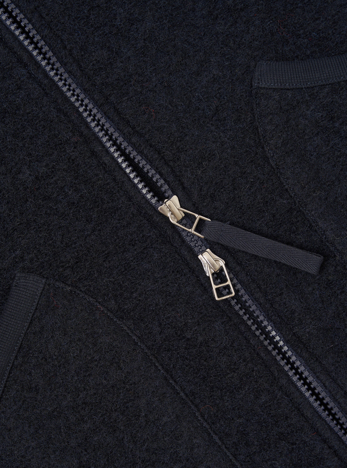 Close-up detail shot of the Navy Wool Fleece Zip Waistcoat on a plain background. Focuses on the metallic front zipper hardware, rounded collar edge, and rich navy blue fleece texture of the garment.