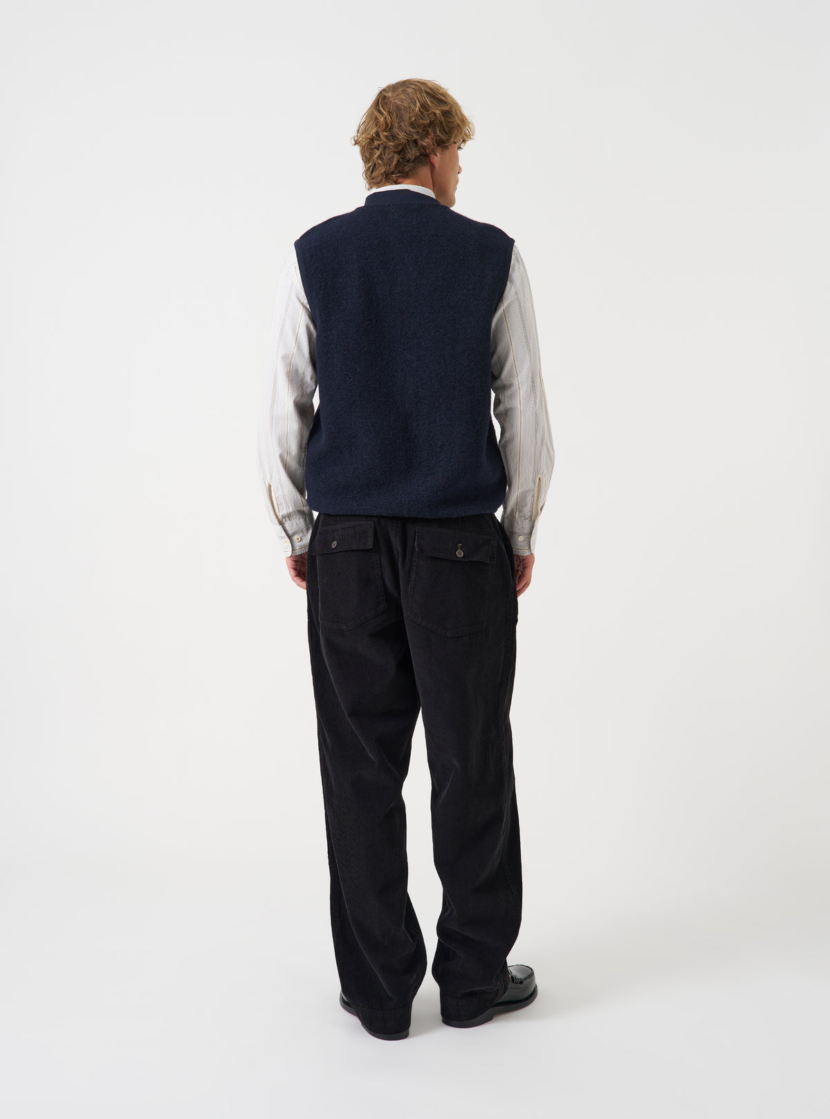 Angled view of a model wearing the Navy Wool Fleece Zip Waistcoat in a plain studio setting. The shot demonstrates the garment fit from the side, highlighting the armhole cut and navy wool fleece texture.