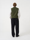 Angled view of a model wearing the Olive Wool Fleece Zip Waistcoat in a plain studio setting. The shot demonstrates the fit from the side, highlighting the armhole cut and textured green fleece fabric.