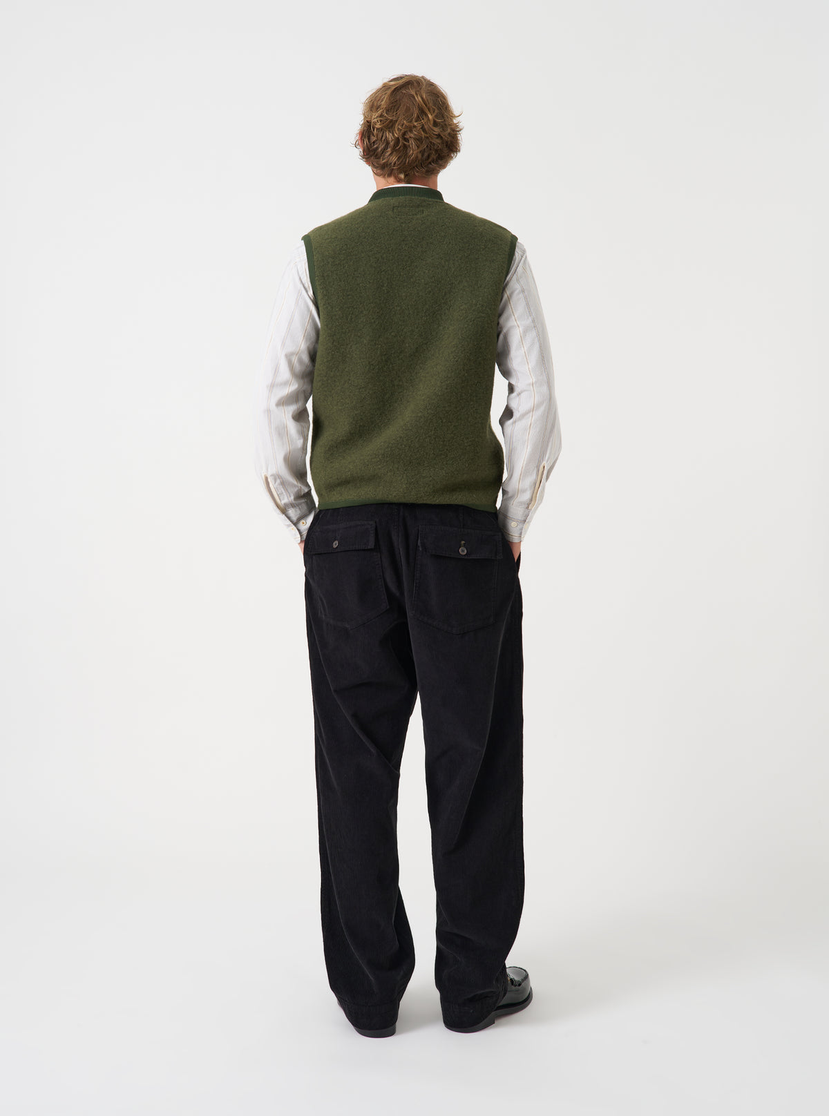 Angled view of a model wearing the Olive Wool Fleece Zip Waistcoat in a plain studio setting. The shot demonstrates the fit from the side, highlighting the armhole cut and textured green fleece fabric.