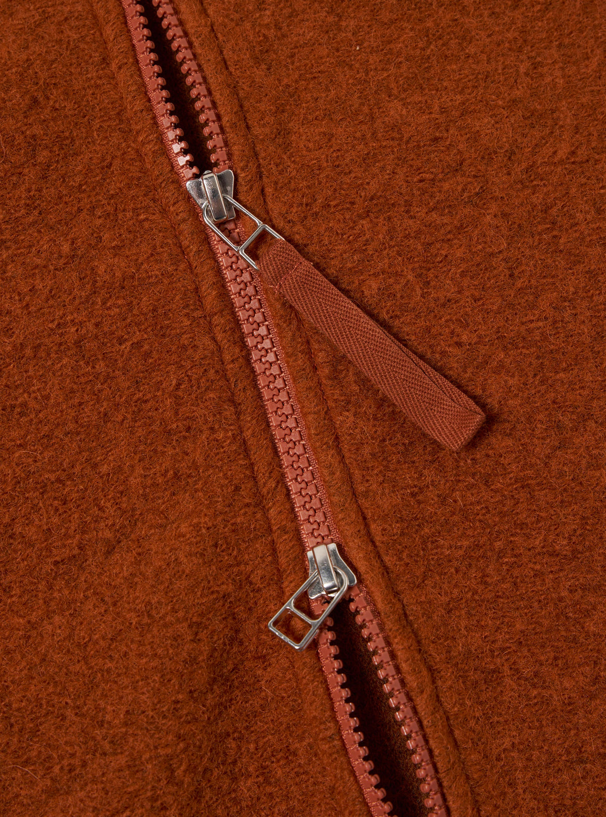 Close-up of the rust-colored wool fleece zip waistcoat, showing the texture of the fleece and the zipper detail. The Rust Wool Fleece Zip Waistcoat is stylish and warm.