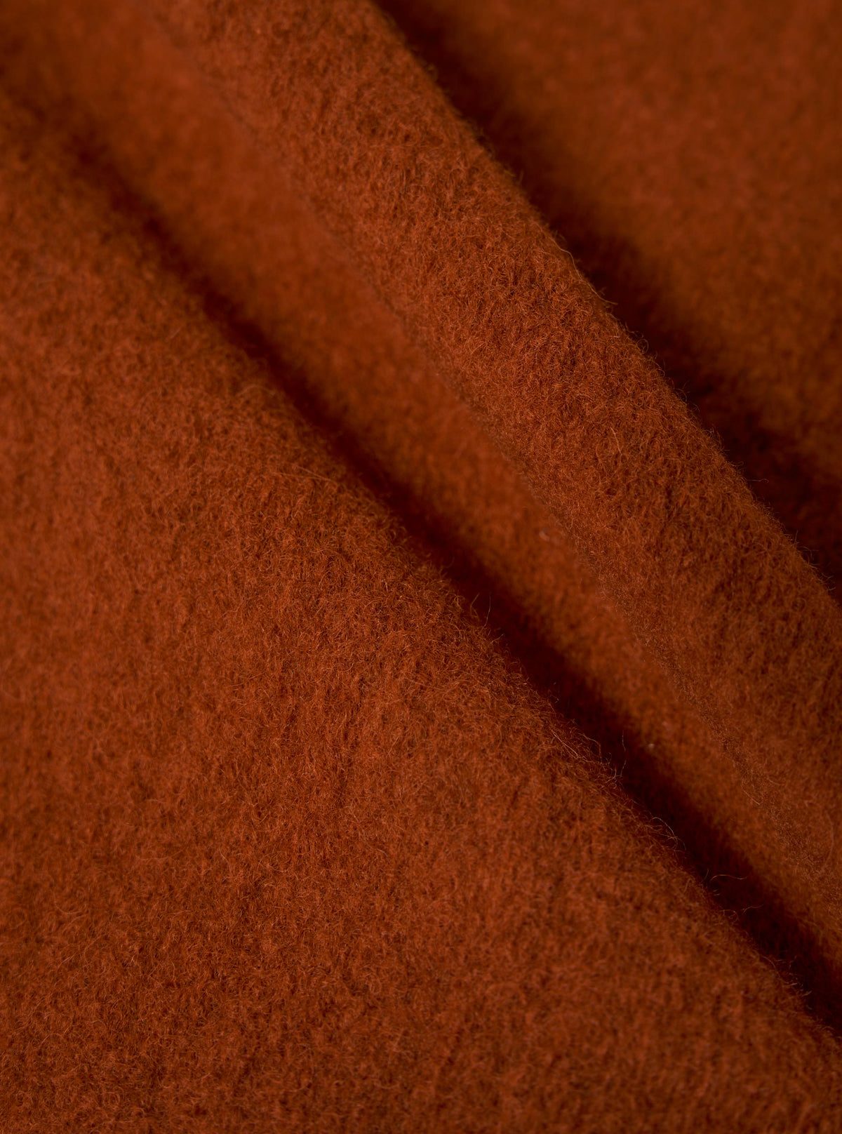 Close-up of the rust-colored wool fleece fabric of the Zip Waistcoat. The soft material is draped to show texture. 