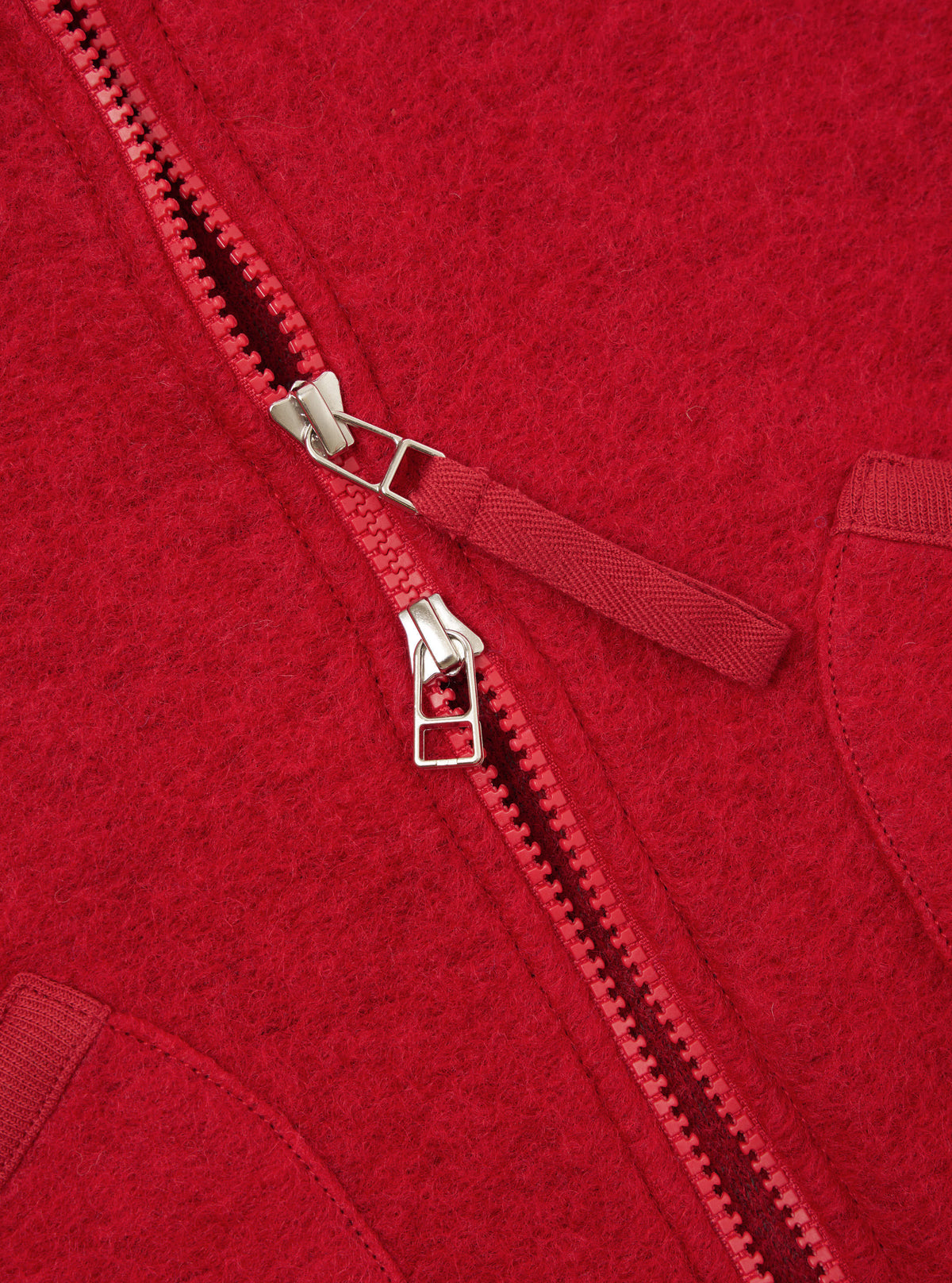 Close-up detail shot of the Scarlet Wool Fleece Zip Waistcoat on a plain background. Focuses on the metallic front zipper hardware, rounded neck trim, and vibrant scarlet red fleece texture of the garment.