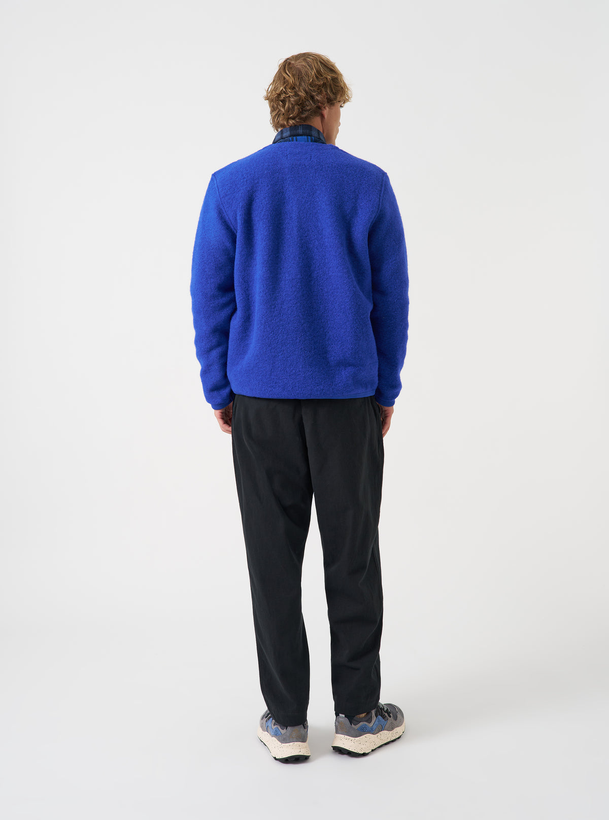 Angled view of a model wearing the Blue Wool Fleece Cardigan in a plain studio setting. The image demonstrates the side profile fit, sleeve structure, and rich blue tone of the cozy fleece fabric.