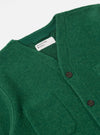 Close-up of a Green Wool Fleece Cardigan on a white surface. The cardigan has brown buttons and a visible tag. The wool has a textured, slightly fuzzy appearance.