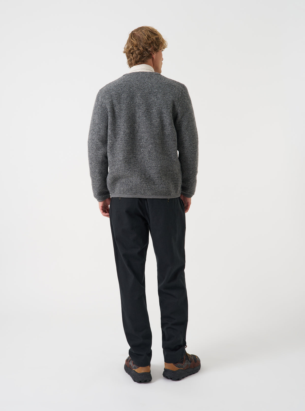 Angled view of a model wearing the Grey Marl Wool Fleece Cardigan in a studio setting. The shot shows the fit from the side, highlighting the textured grey marl fleece fabric, ribbed cuffs, and side pocket.