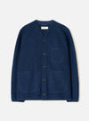Indigo wool fleece cardigan laid flat on a light grey studio backdrop. V-neckline with a woven Universal Works label at the back neck. Five dark horn buttons down the front placket. Four patch pockets, two chest and two hip. Textured boiled wool fleece fabric. Straight hem and full-length sleeves.