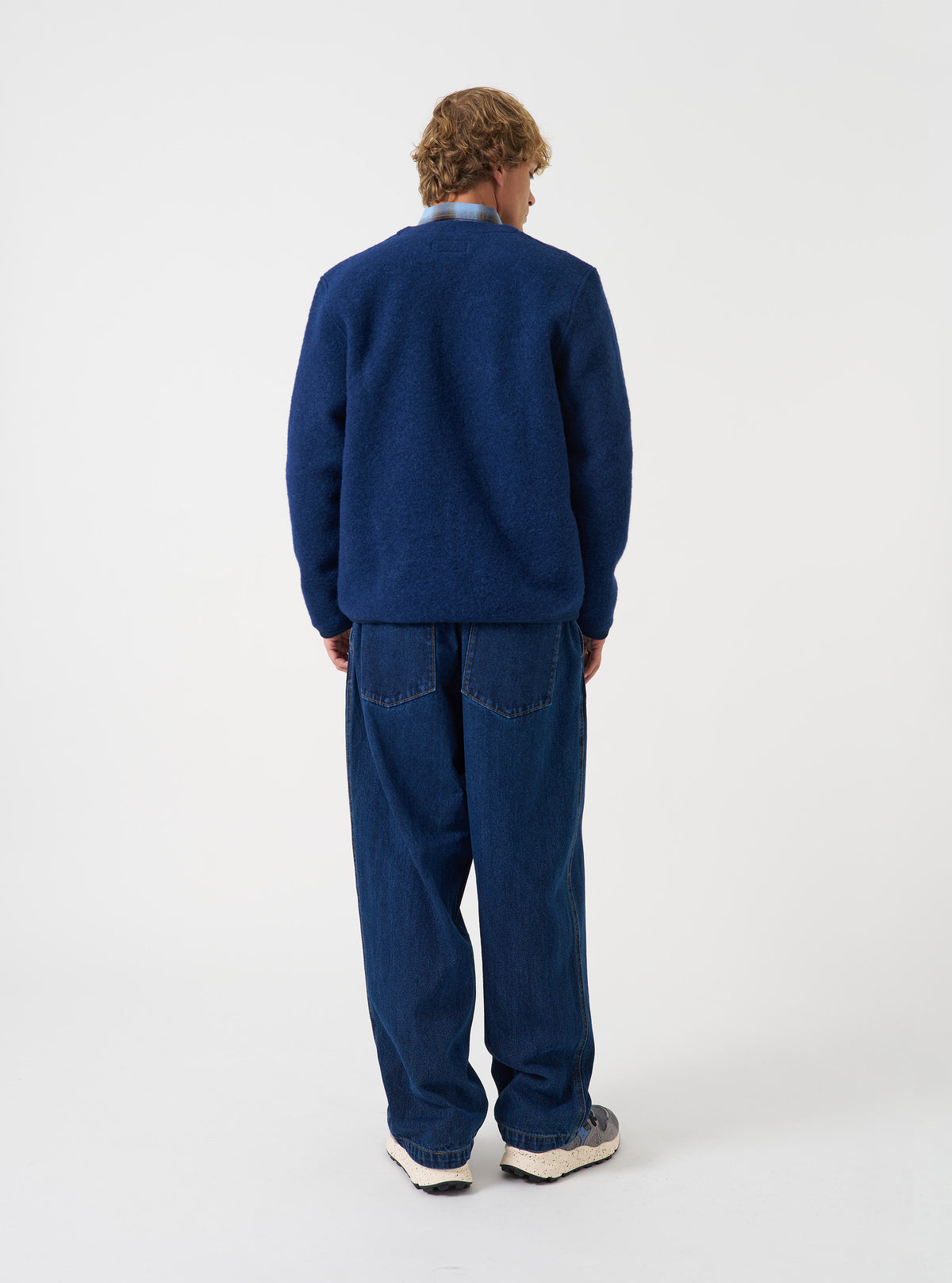 Angled view of a model wearing the Indigo Wool Fleece Cardigan in a plain studio setup. The image demonstrates the relaxed fit, cuff ribbing, and rich indigo blue wool fleece texture from the side.