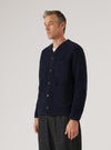 A man poses in profile against a white backdrop, wearing a Navy Wool Fleece Cardigan with button closure and patch pockets. The cardigan is paired with dark trousers.