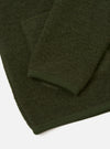 Close-up flat lay of an olive wool fleece cardigan on a white studio surface. The boiled wool texture is visible across the body and sleeve. A ribbed knit cuff in matching olive sits at the sleeve end, with the hem also finished in the same tonal ribbed trim.