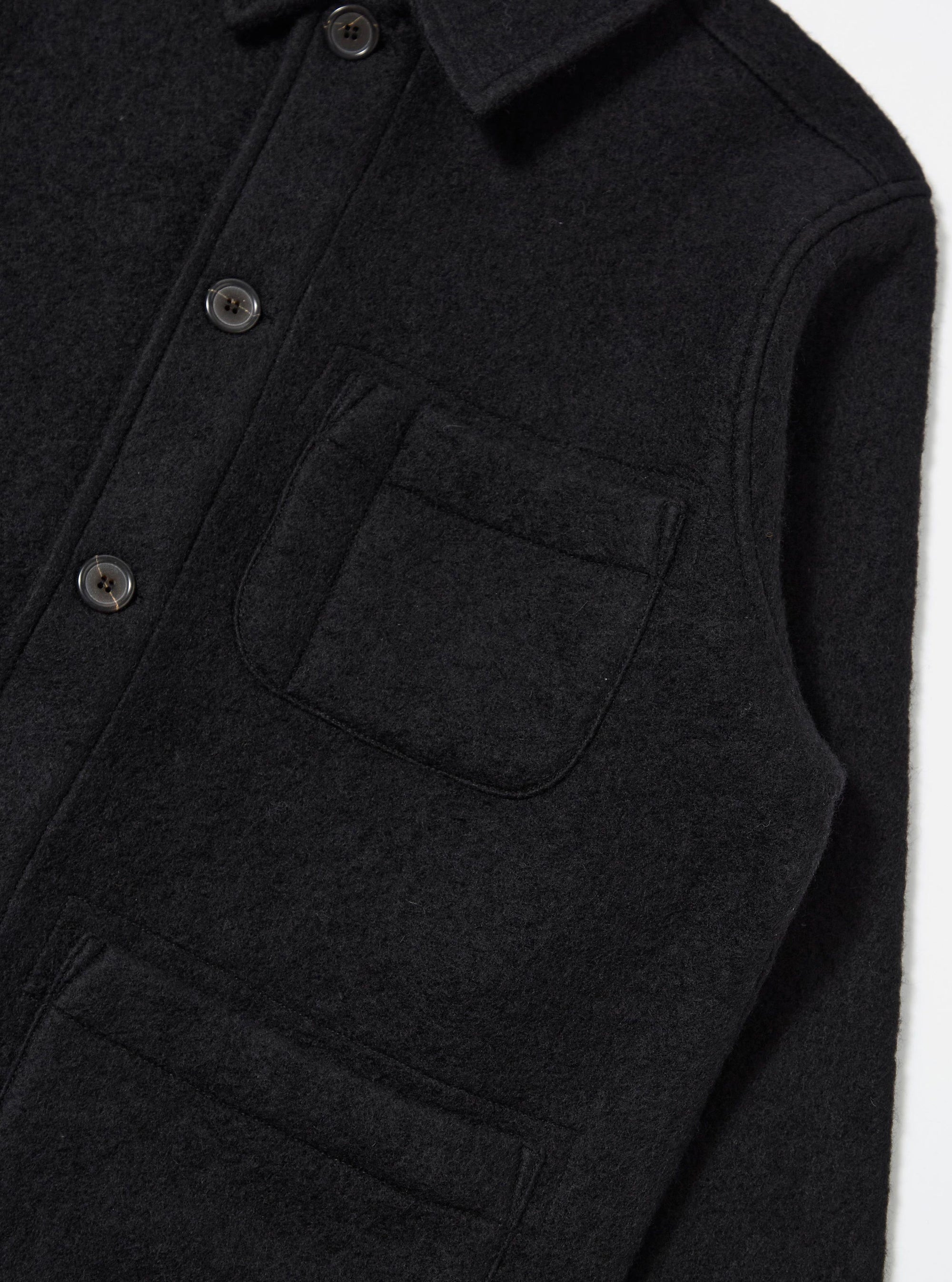 Close-up of the Black Wool Fleece Field Jacket. The jacket is black wool with button closure and chest pockets. Shot against a white backdrop.