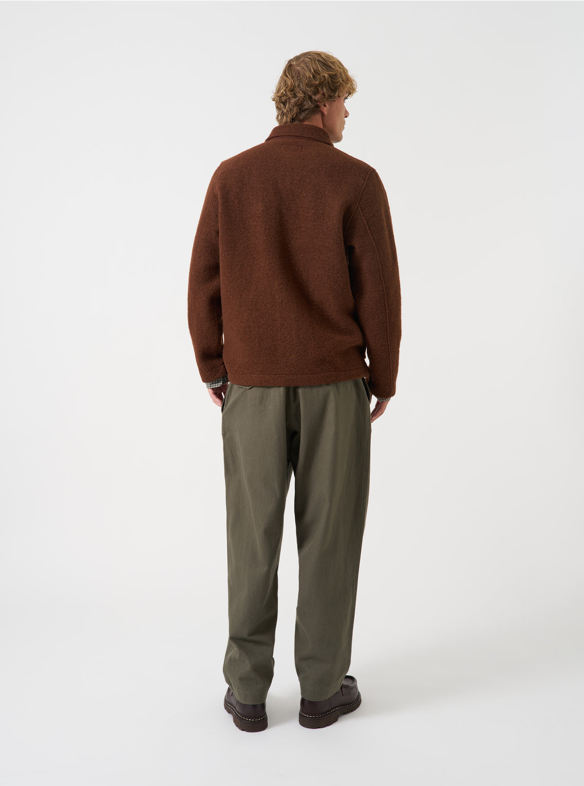 Angled rear view of a model wearing the Cacao Wool Fleece Field Jacket in a plain studio setting, showcasing the overall fit from the back and side in rich cacao brown wool fleece.