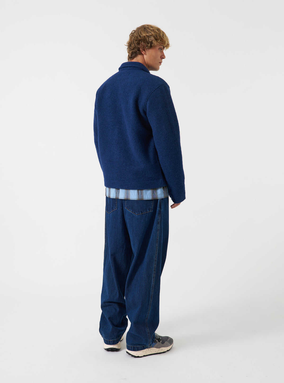 Side view of a model wearing the Indigo Wool Fleece Field Jacket in a plain studio environment. The image displays the fit along the arms, shoulder line, and side profile of the blue wool fleece garment.