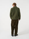 Angled view of a model wearing the Olive Wool Fleece Field Jacket in a studio setting. The model turns slightly, showing the fit, sleeve length, and rich olive green wool fleece material from a side perspective.