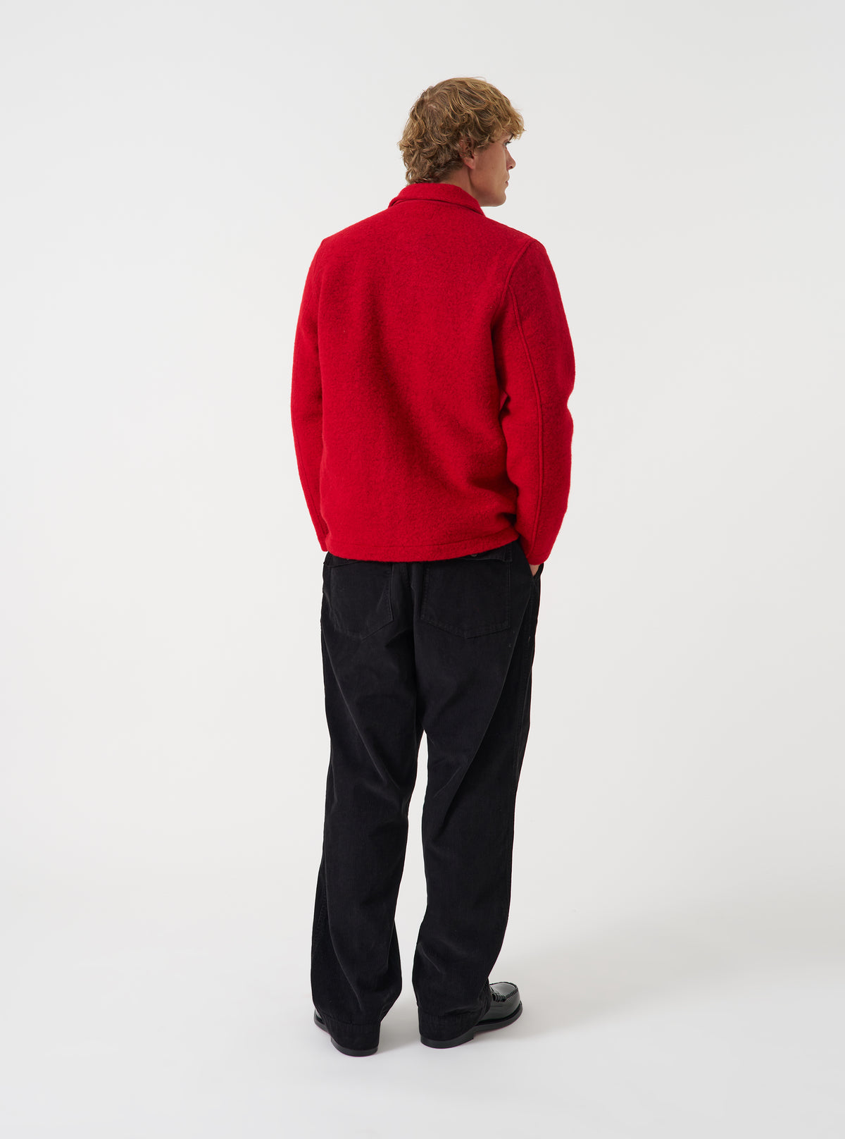Angled side view of a model wearing the Scarlet Wool Fleece Field Jacket in a plain studio setting. Demonstrates the garment fit, side profile, chest pocket detail, and scarlet red fleece texture.