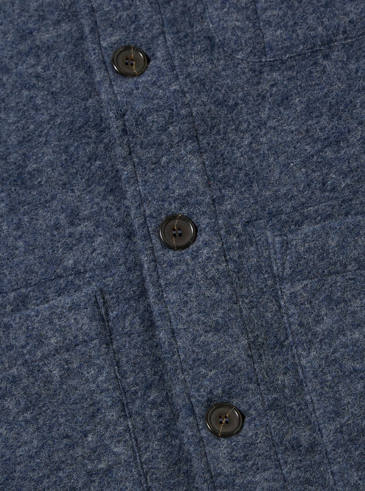 Close-up of the slate blue wool fleece field jacket, showing the texture of the wool and the button details. The jacket is laid flat on a neutral surface.