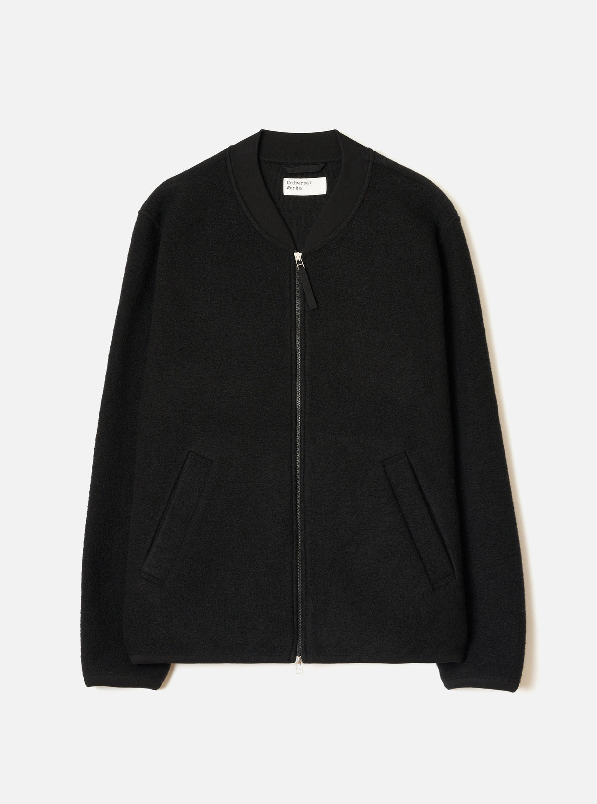 Black wool fleece zip bomber jacket, flat lay on a light grey seamless backdrop. Ribbed bomber collar with a Universal Works label visible at the neckline. Full-length silver zip with a leather pull tab. Textured boiled wool fleece body, two front welt pockets, and ribbed cuffs at the hem of each sleeve.