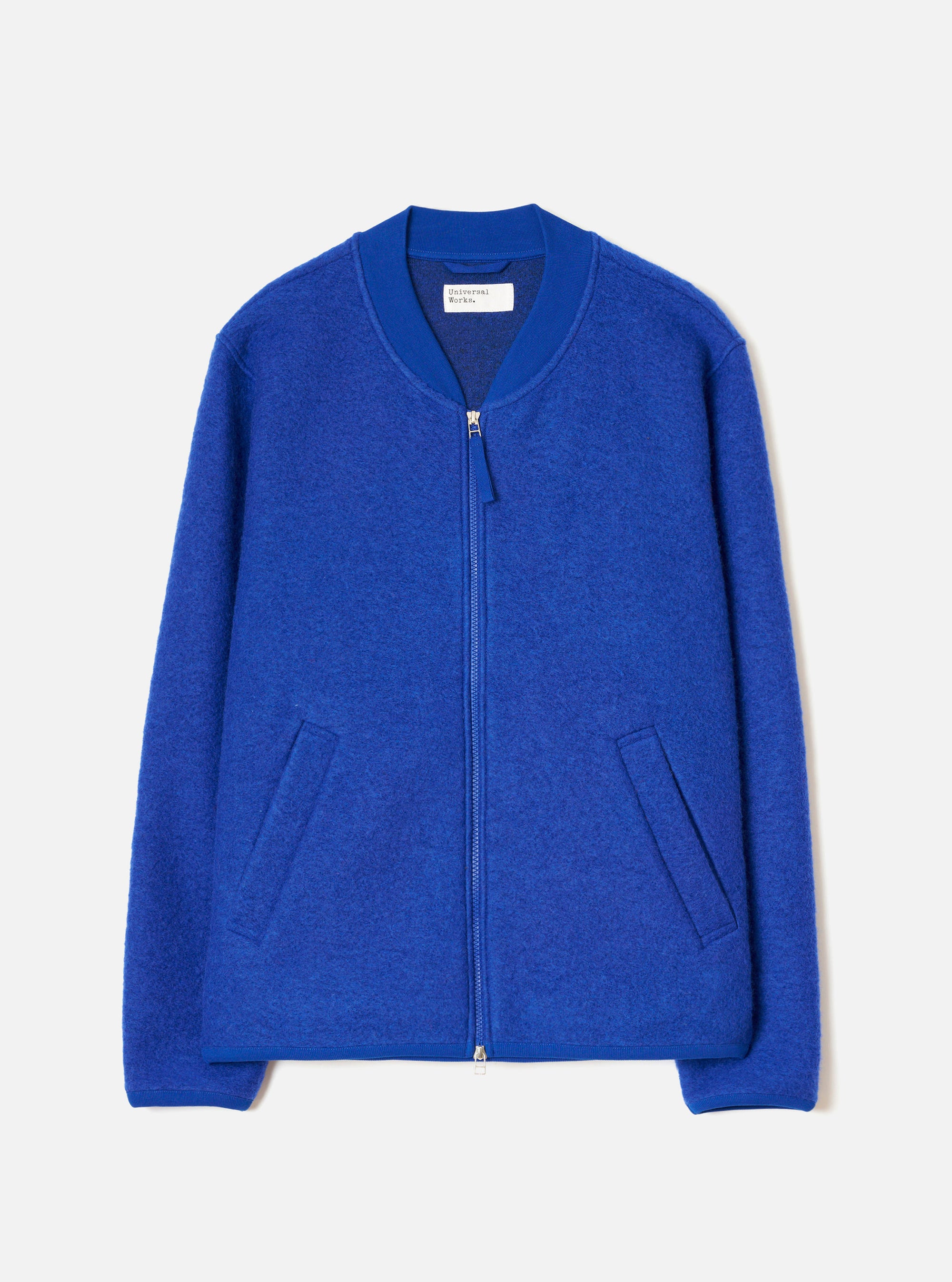 Blue wool fleece zip bomber on a plain light grey studio backdrop, no model. The jacket features a ribbed bomber collar, a central silver zip with a fabric pull tab, two welt hand pockets at the hip, and ribbed cuffs and hem. The textured wool fleece has a softly boiled finish throughout.