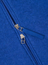 Close-up detail of the double zip fastening on a blue wool fleece zip bomber. Two gold-tone metal zip sliders sit on blue plastic teeth, with a woven blue zip pull tab. The brushed wool fleece texture is visible across the royal blue fabric.