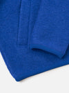Close-up flat lay of a blue wool fleece zip bomber on a white surface. The textured boiled wool fabric is shown in detail alongside a ribbed knit cuff at the sleeve end and a matching ribbed hem. A front zip placket is visible at the top left of the frame.