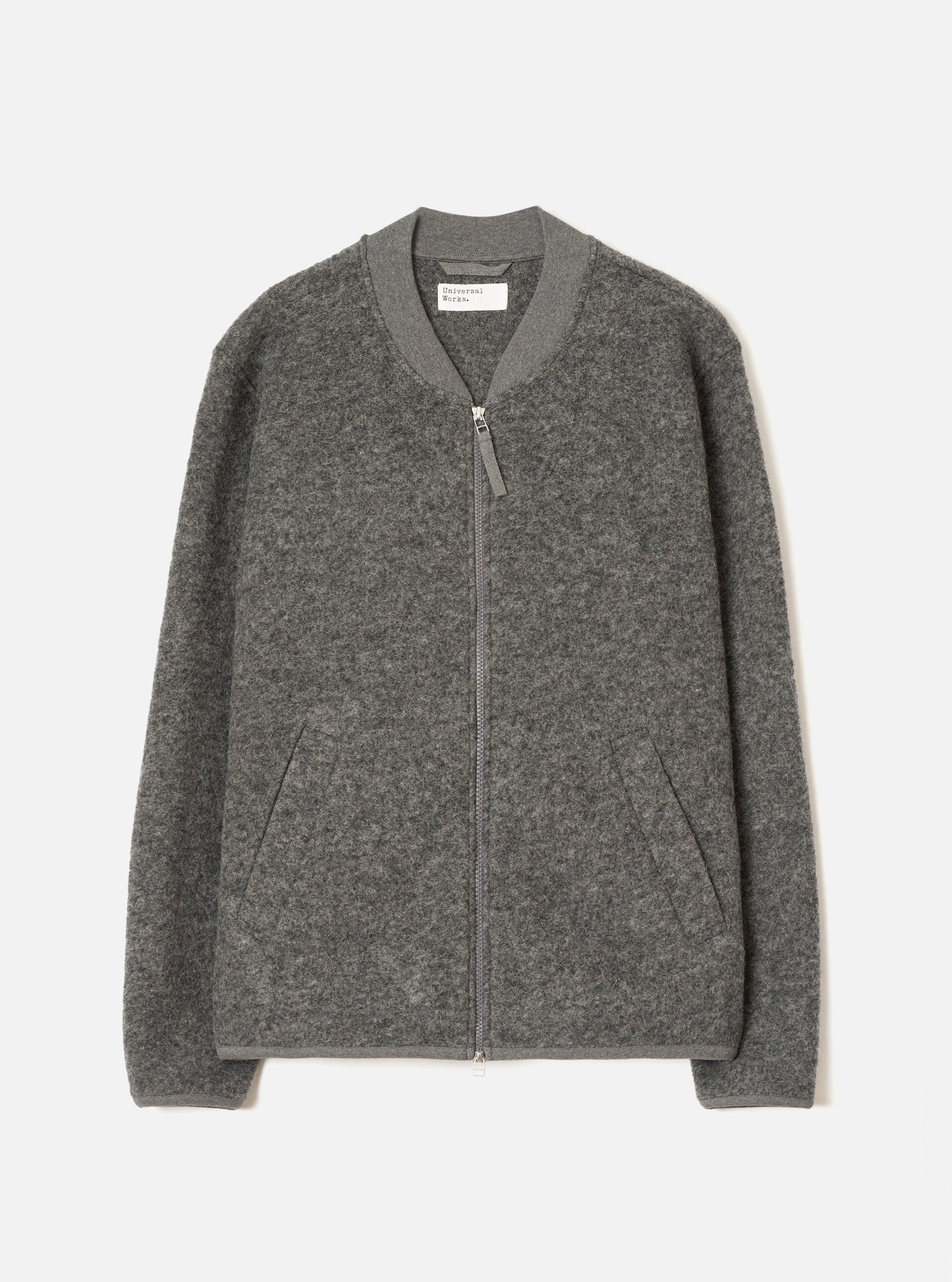 Grey marl wool fleece zip bomber, flat lay on a light grey seamless backdrop. Ribbed bomber collar with a centre-front silver zip and leather zip pull. Two welt hand pockets at the hem. Ribbed cuffs and hem band. Textured boiled wool fleece fabric throughout. Universal Works label visible at the inner collar.