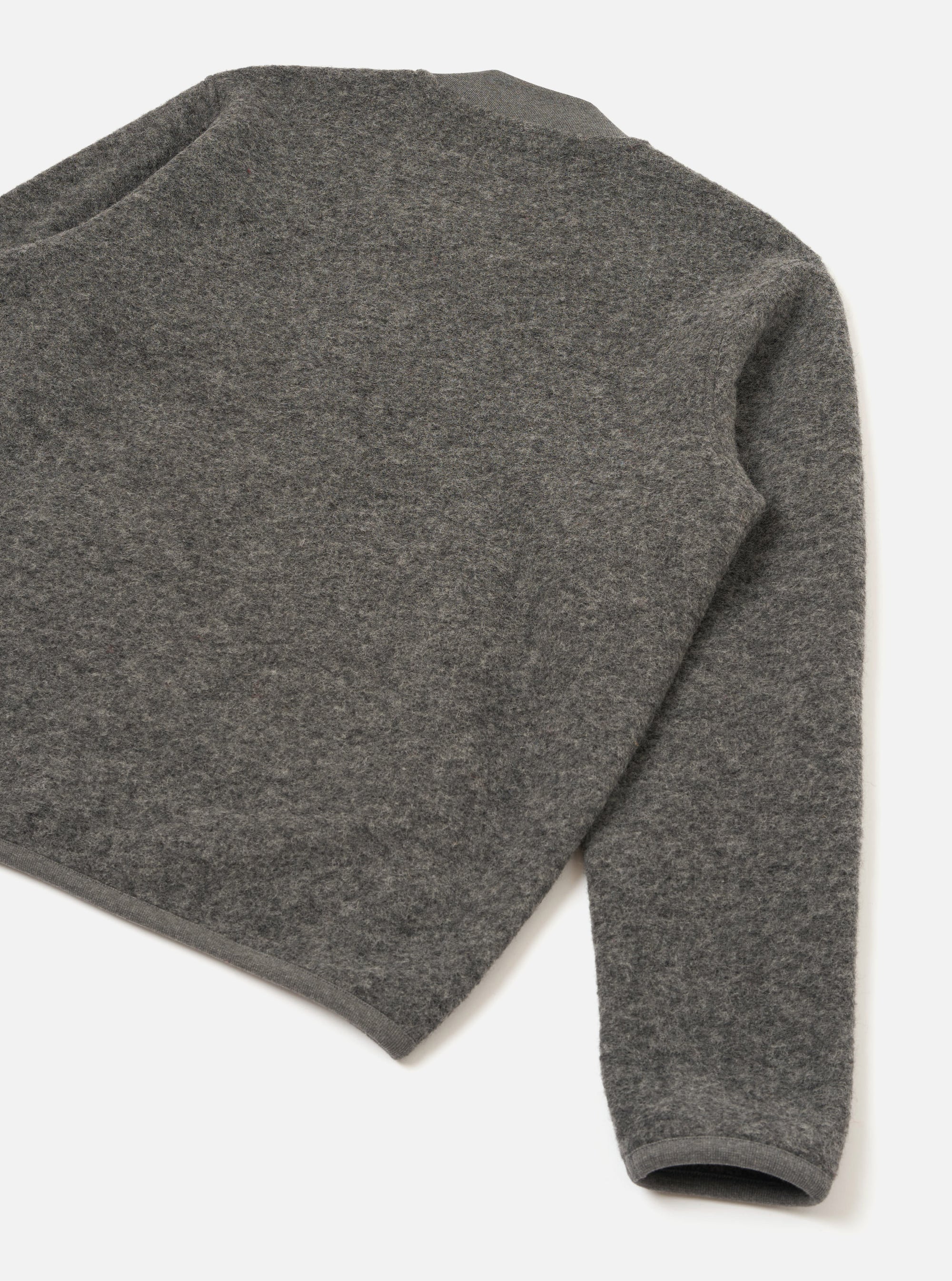 Grey marl wool fleece zip bomber, flat lay on a white surface, angled shot showing the back body and one sleeve. The boiled wool fleece has a dense, nubby texture throughout. A ribbed cuff is visible at the sleeve hem, with a matching ribbed trim at the neckline and body hem.