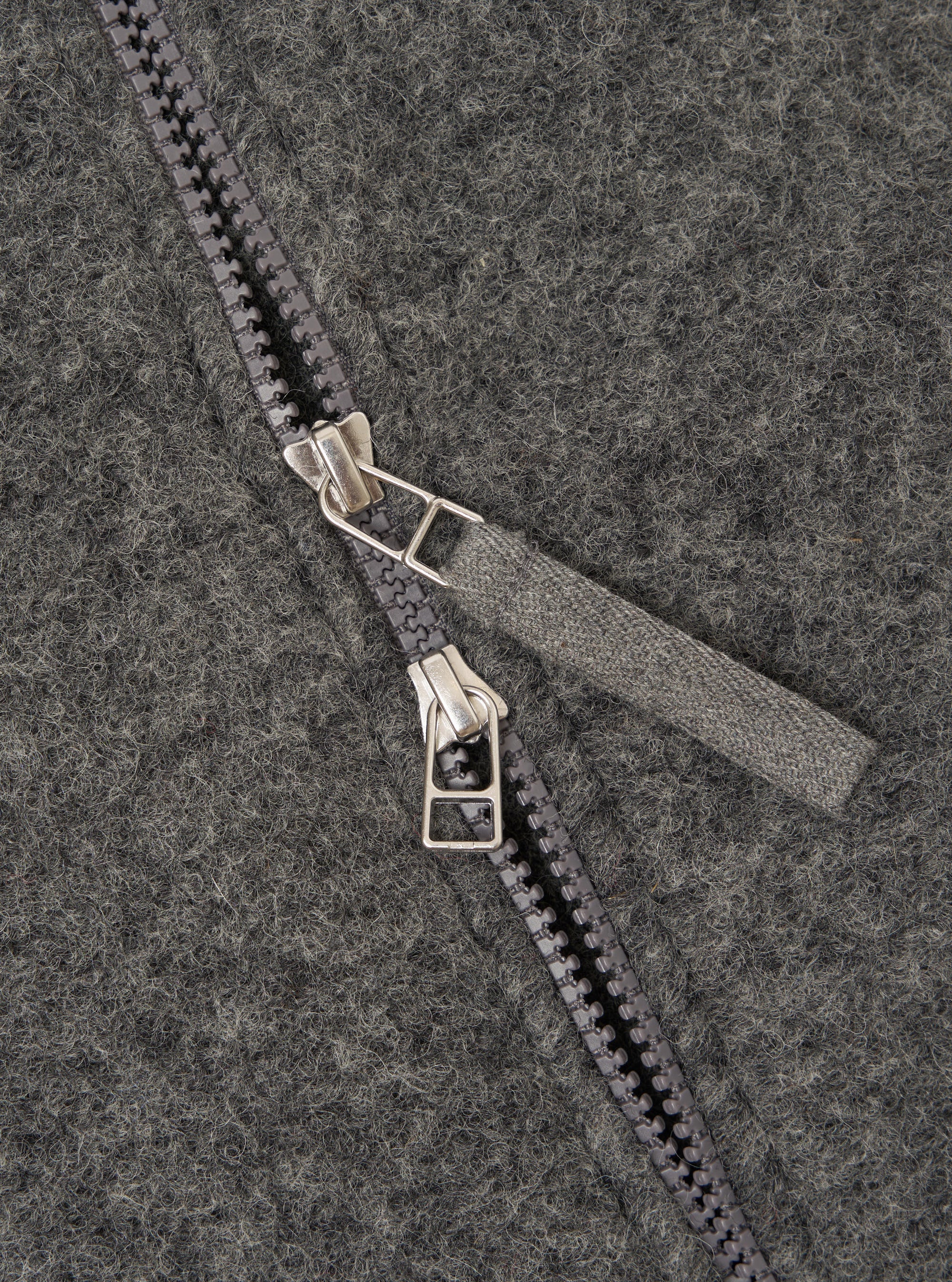 Close-up detail of the grey marl wool fleece zip bomber, showing a two-way gunmetal zip with twin silver-toned sliders and a woven fabric zip garage. The brushed wool fleece texture is visible across the full frame, showing a flecked marl finish.