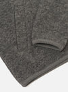 Close-up flat lay of a grey marl wool fleece zip bomber, folded to show the sleeve and hem. The boiled wool fleece has a dense, nubby texture throughout. A ribbed knit cuff is visible at the sleeve end, and a matching ribbed hem strip runs along the bottom edge. Shot on a white studio surface.