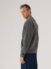 Grey marl wool fleece zip bomber worn by a male model, shot from a three-quarter rear angle against a light grey studio backdrop. The brushed, textured wool fleece fabric is visible across the back and sleeve. A ribbed cuff is visible at the wrist. The bomber is worn untucked over dark navy wide-leg jeans, cropped at mid-thigh.