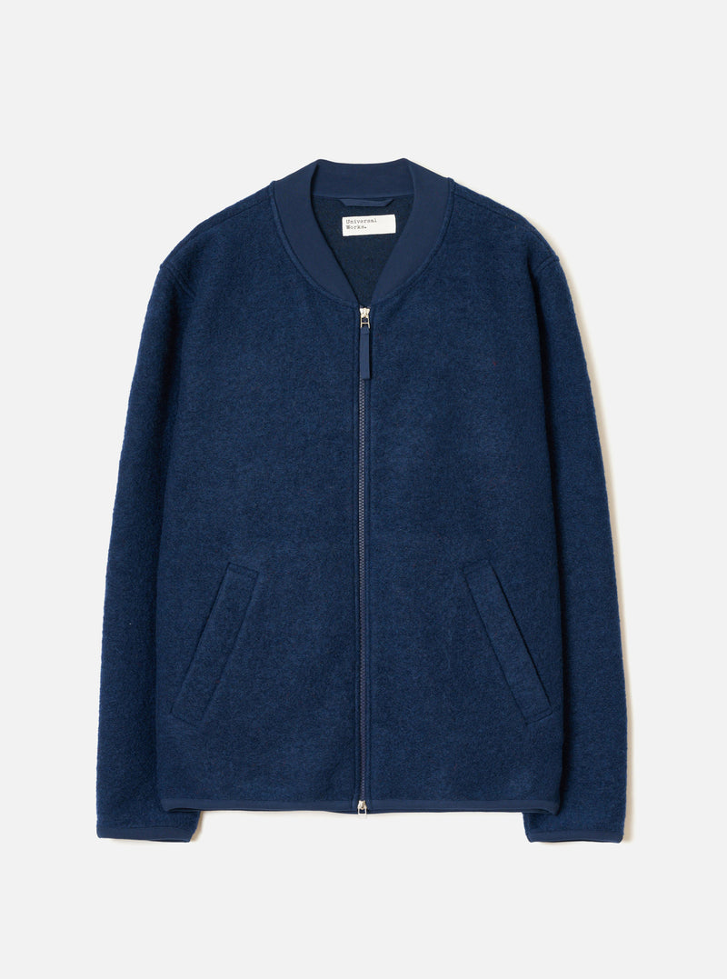 The Indigo Wool Fleece Zip Bomber Jacket is laid flat on a light grey backdrop. Features a ribbed collar, full-length silver zipper, two welt hip pockets, ribbed cuffs, and dense textured boiled wool fleece material.