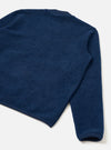 Flat lay of an indigo wool fleece zip bomber on a white studio surface, shot from above at an angle. The back and one sleeve are visible, showing a dense, brushed wool fleece texture. Navy bound seams run along the armhole and hem. The cuff is finished with a matching navy ribbed band.