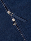 Close-up detail of the dual zip fastening on an indigo wool fleece bomber. Two silver-tone zip sliders sit together on a navy plastic-tooth zip, with a woven navy fabric pull tab. The boiled wool fleece texture is visible across the frame.