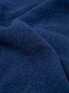 Close-up of indigo wool fleece fabric, showing a dense, brushed texture with fine curling fibres and a lightly boiled surface. The deep navy-indigo tone has subtle variation across the folds and creases of the cloth. No garment details or background are visible.