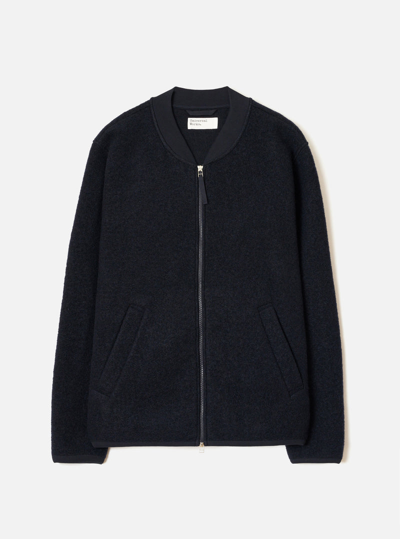 The Navy Wool Fleece Zip Bomber Jacket is laid flat on a light grey seamless backdrop. Details include a textured boiled-wool fleece body, smooth ribbed bomber collar, full-length silver zipper with pull tab, two welt pockets, and ribbed hem and cuffs.