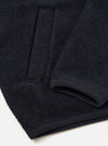 Close-up flat lay of a navy wool fleece zip bomber on a white surface. The boiled wool texture is clearly visible. The shot shows the lower front panel, a chest welt pocket, the ribbed hem, and a ribbed cuff folded back to reveal its trim detail.