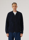 Navy wool fleece zip bomber worn by a male model against a light grey studio backdrop. The jacket is fully zipped, with a silver two-way zip, ribbed bomber collar, and two slanted side pockets. The textured boiled wool fleece fabric is visible throughout. Cropped at the thigh, layered over a white crew-neck tee and dark blue jeans.