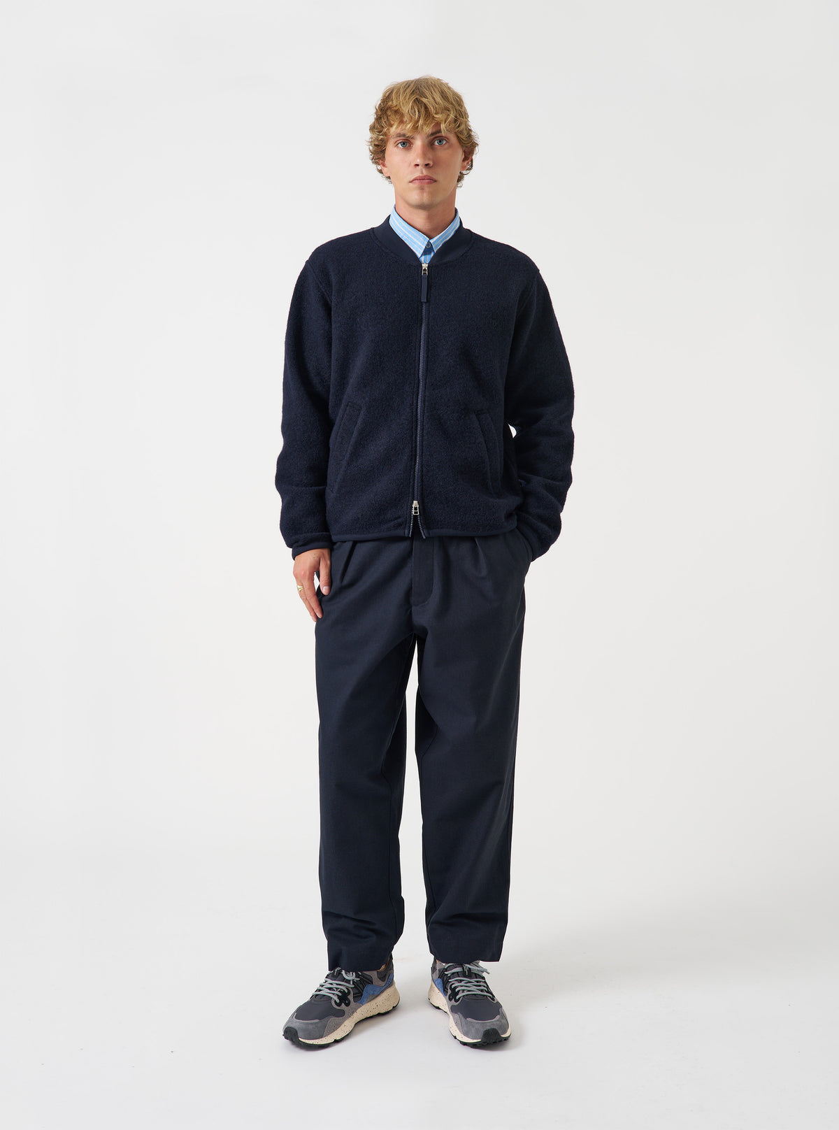 Front view of a model wearing the Navy Wool Fleece Zip Bomber Jacket in a plain studio setting. The model stands facing forward, showing the dark navy blue wool fleece jacket, front zipper, and casual style fit.