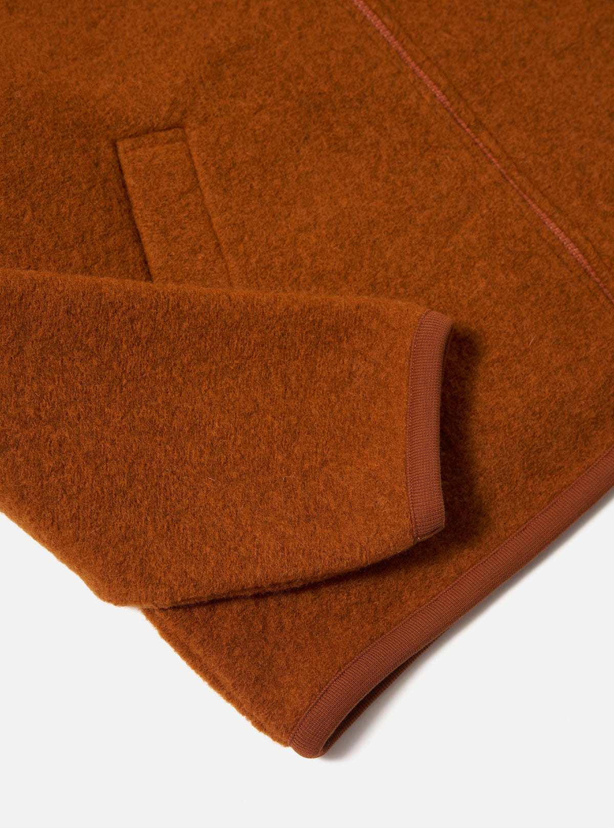 Close-up of the Rust Wool Fleece Zip Bomber showing the rust-colored wool fleece material and ribbed trim on a white background.