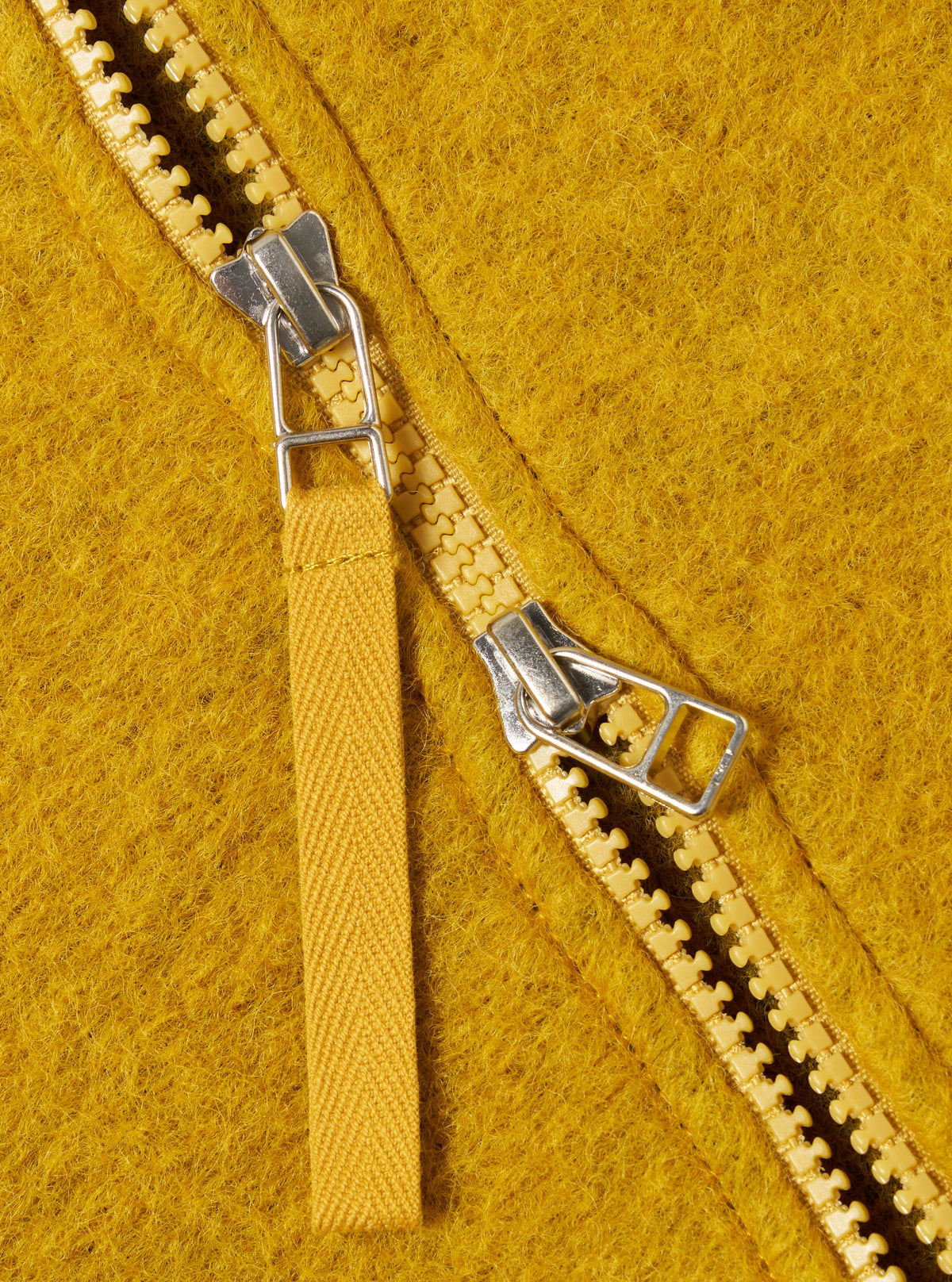 Close-up of the Yellow Wool Fleece Zip Bomber, showcasing the texture of the wool and the zipper detail. The background is a plain surface.