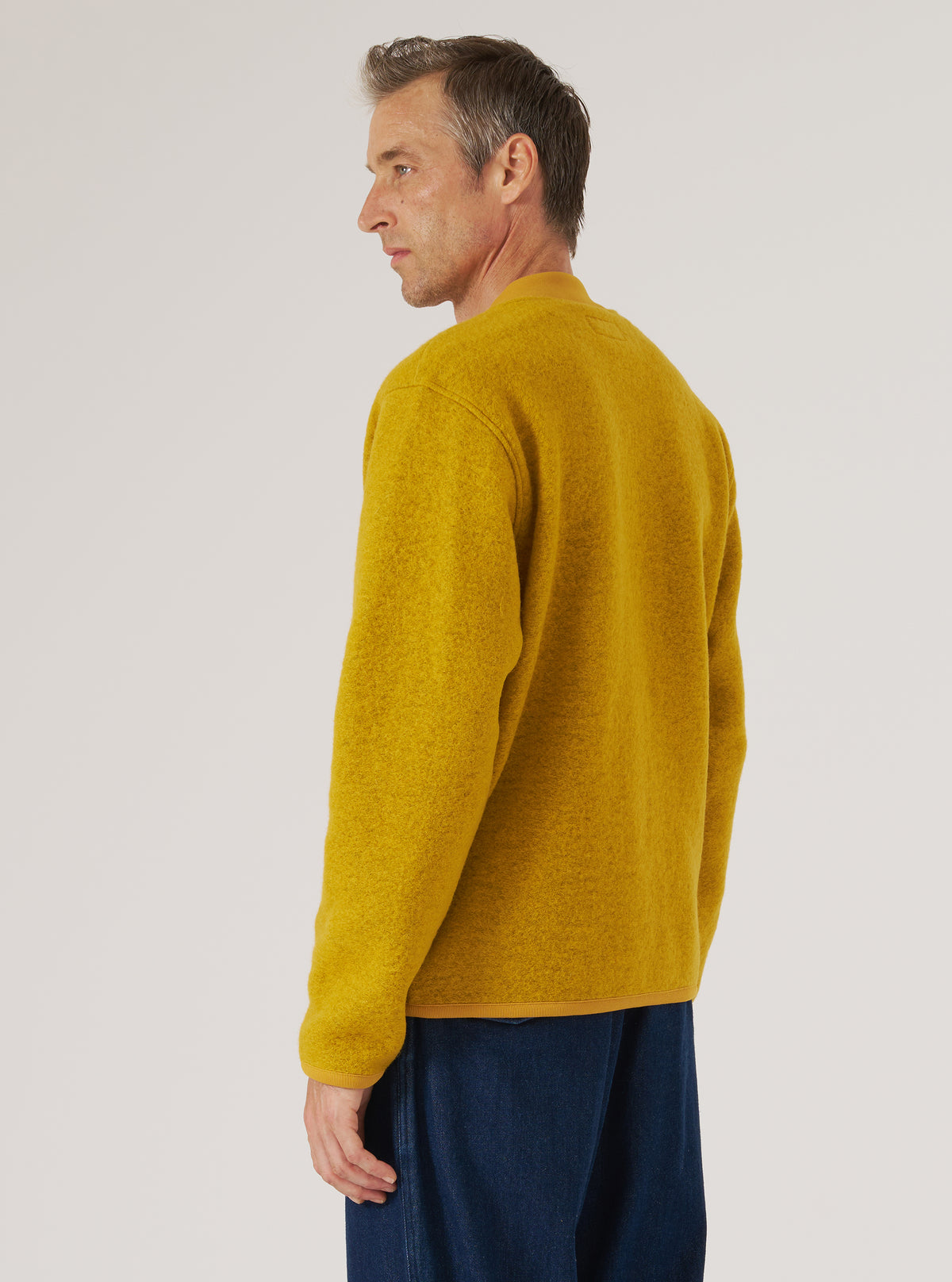A man models the Yellow Wool Fleece Zip Bomber against a plain backdrop. The bomber is a vibrant yellow, made of wool fleece, and has a zip front. The fit is relaxed and casual.