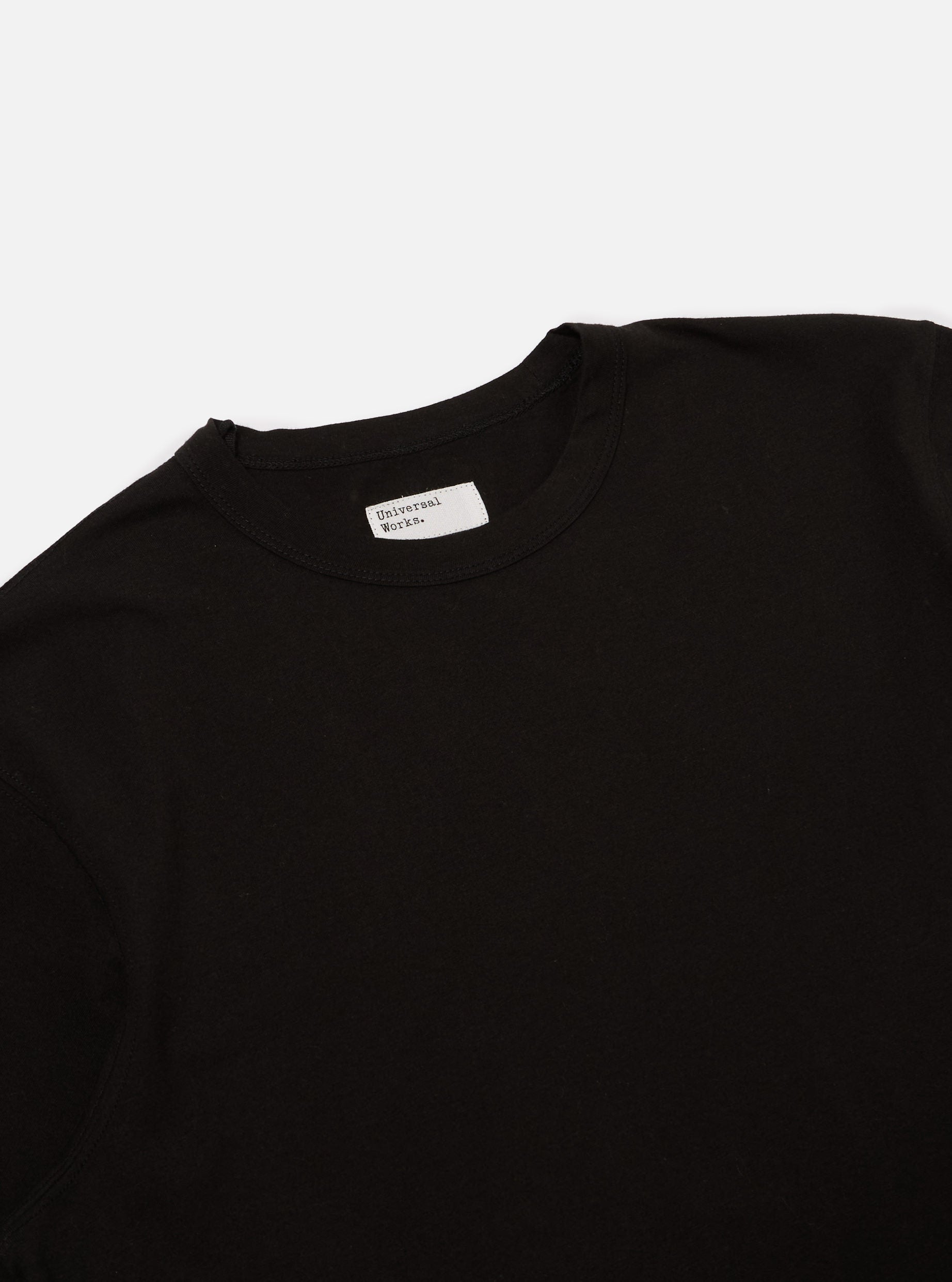 Close-up of a Black Single Jersey Core Tee on a white background. The simple tee shows the collar and upper chest area.