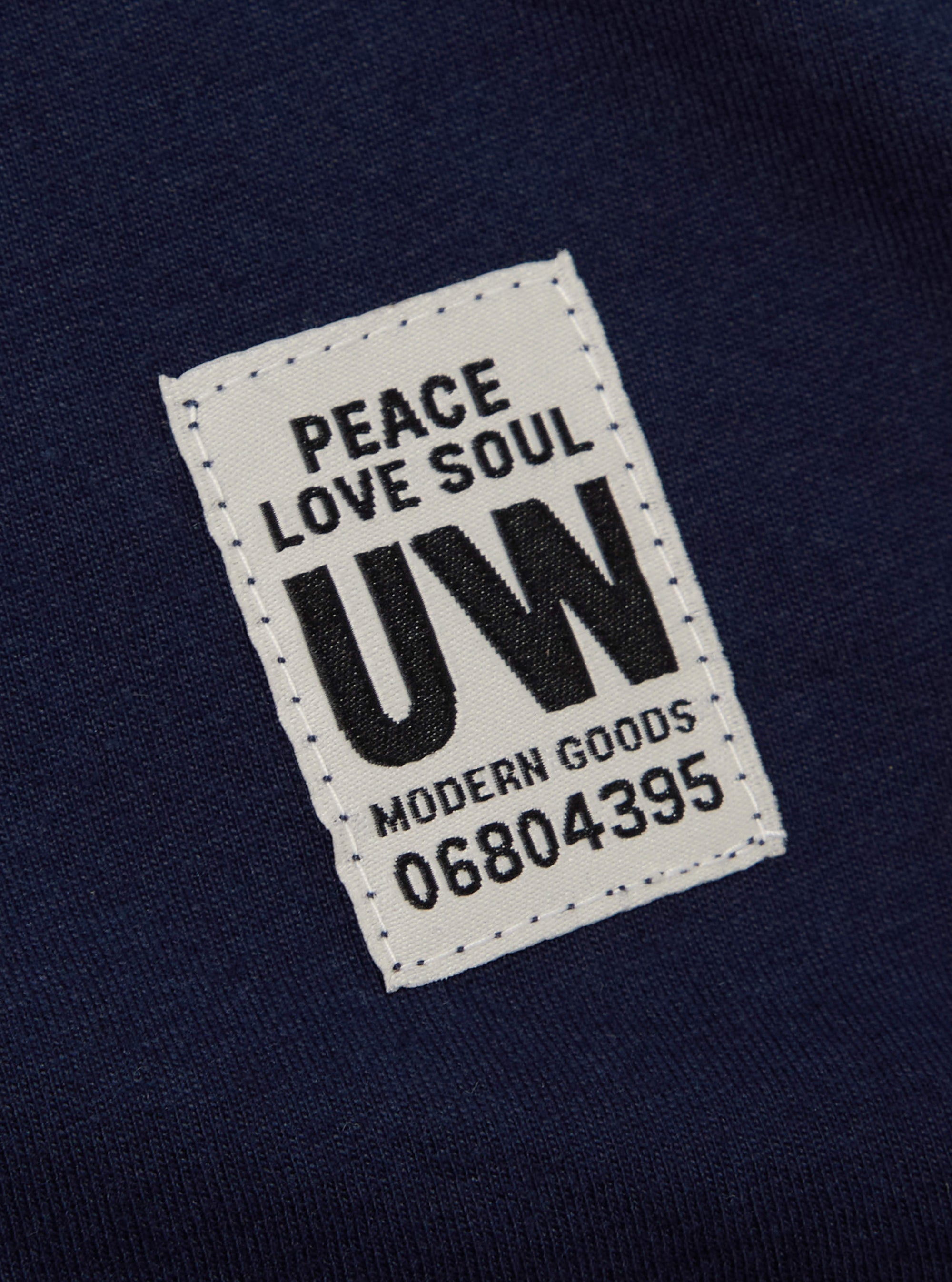 Close-up of the Navy Single Jersey Core Tee showing the fabric and a tag with "Peace Love Soul UW Modern Goods 06804395" on it.