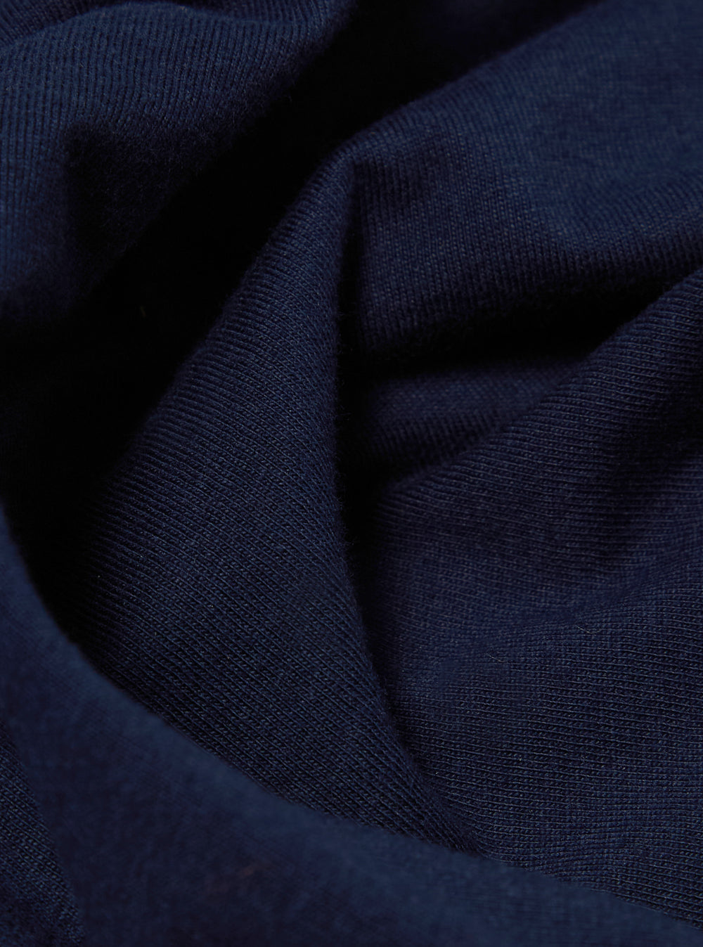 Close-up of the Navy Single Jersey Core Tee fabric. The soft, textured material is draped on a flat surface, showcasing its rich navy color and fine knit.